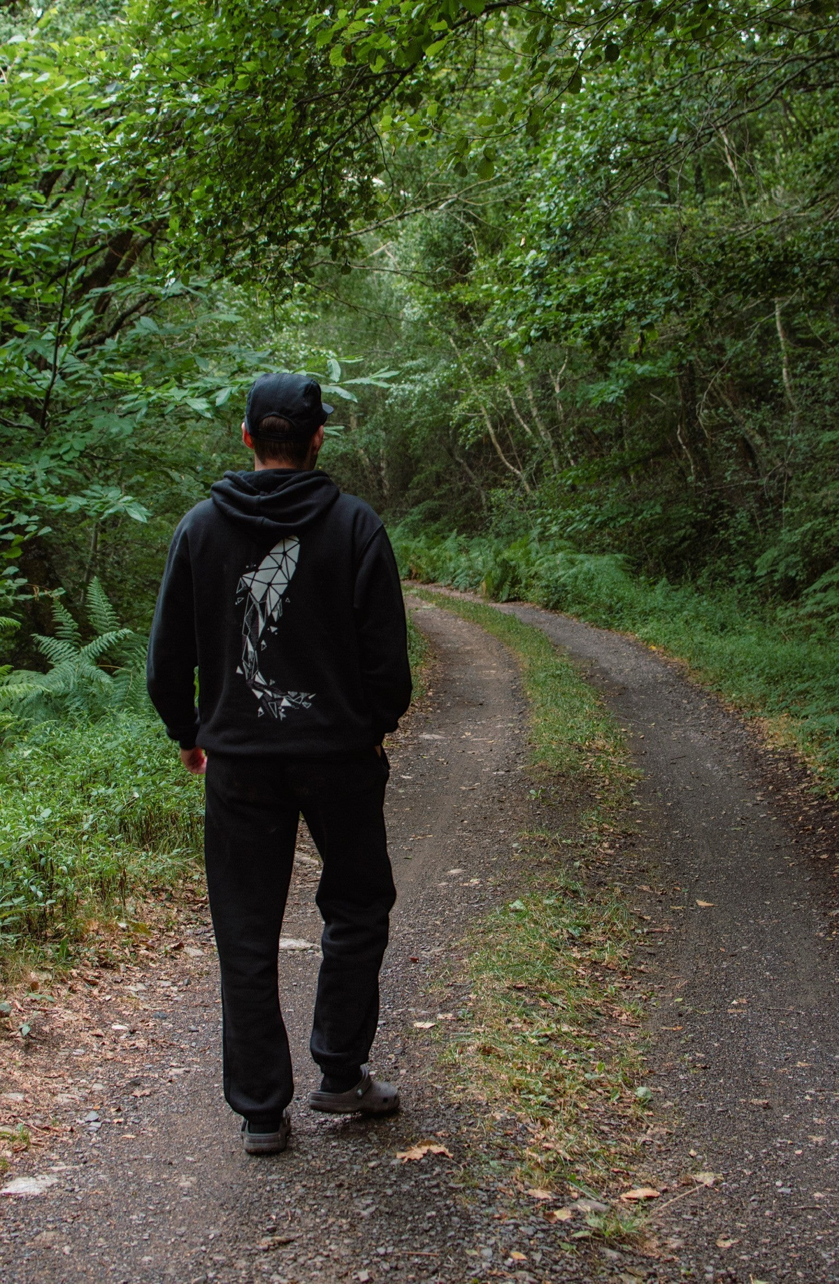 Connected Carper black hoodie with geometric carp print on back, worn by a man walking on a forest path.