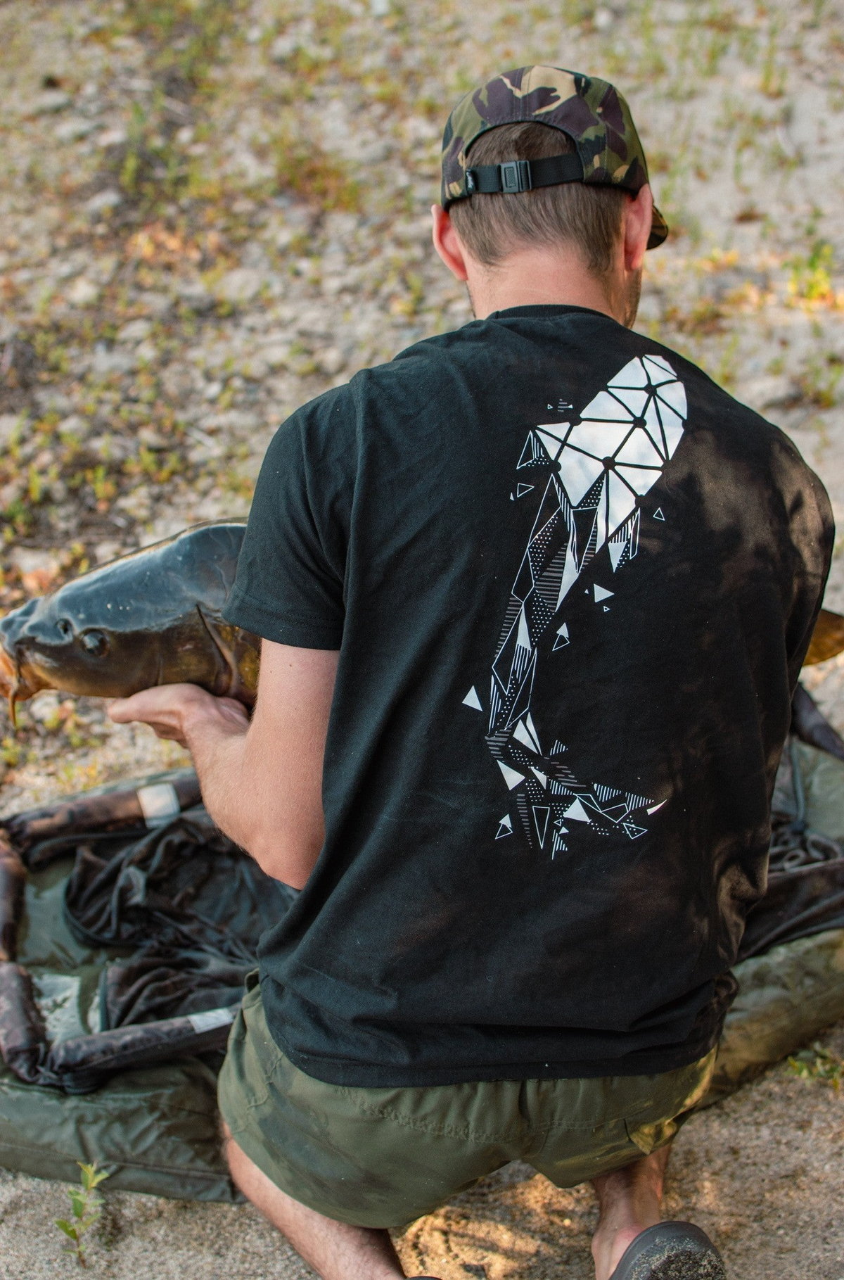 Connected Carper black cotton t-shirt with a large white geometric carp design on the back worn by a fisherman