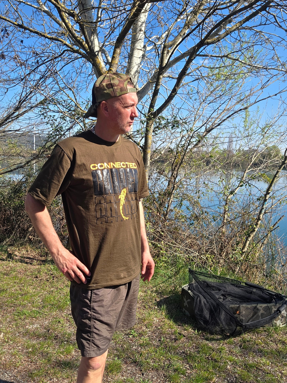 Connected Carper khaki cotton-blend t-shirt with orange logo, worn by a man outdoors by a lake.