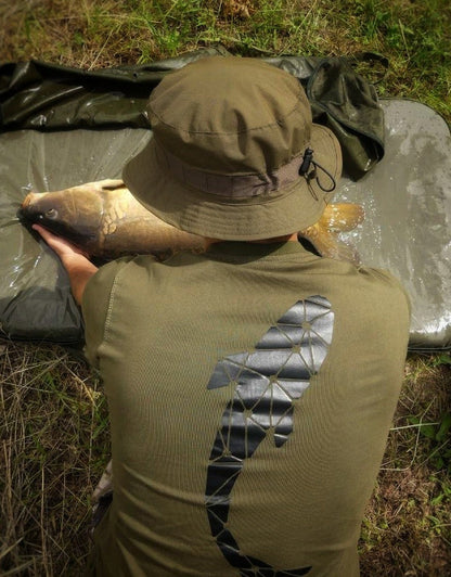 Connected Carper khaki fishing t-shirt with geometric carp logo, worn by an angler holding a carp at the water's edge.