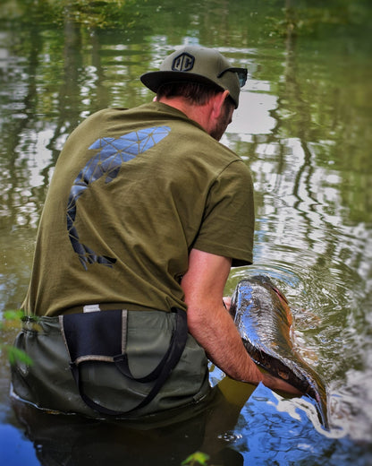 Connected Carper khaki fishing t-shirt with carp logo on back, worn by a man releasing a fish in a lake.