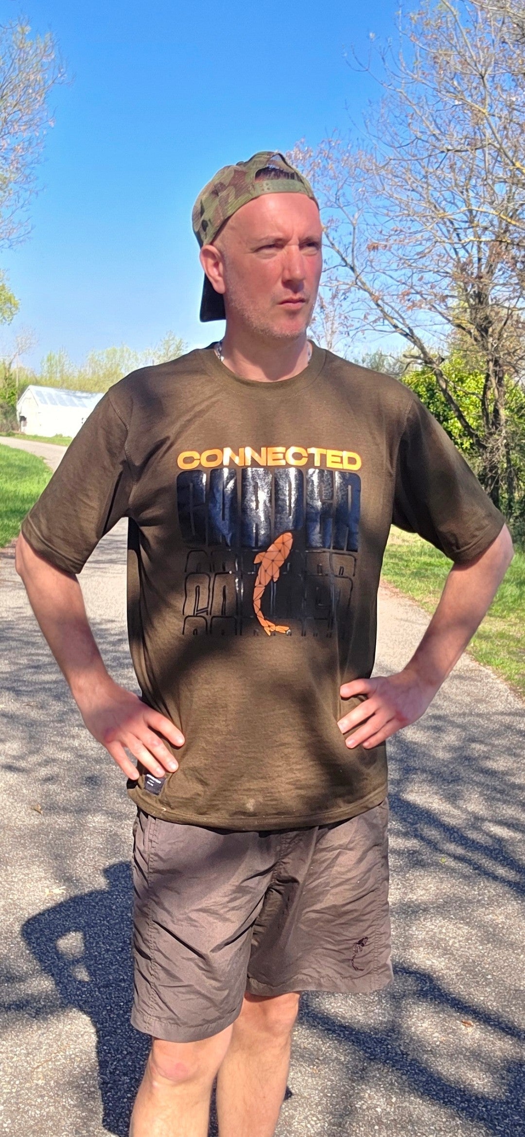 Connected Carper khaki cotton-blend t-shirt with orange logo, worn by a man outdoors in a casual fishing setting.