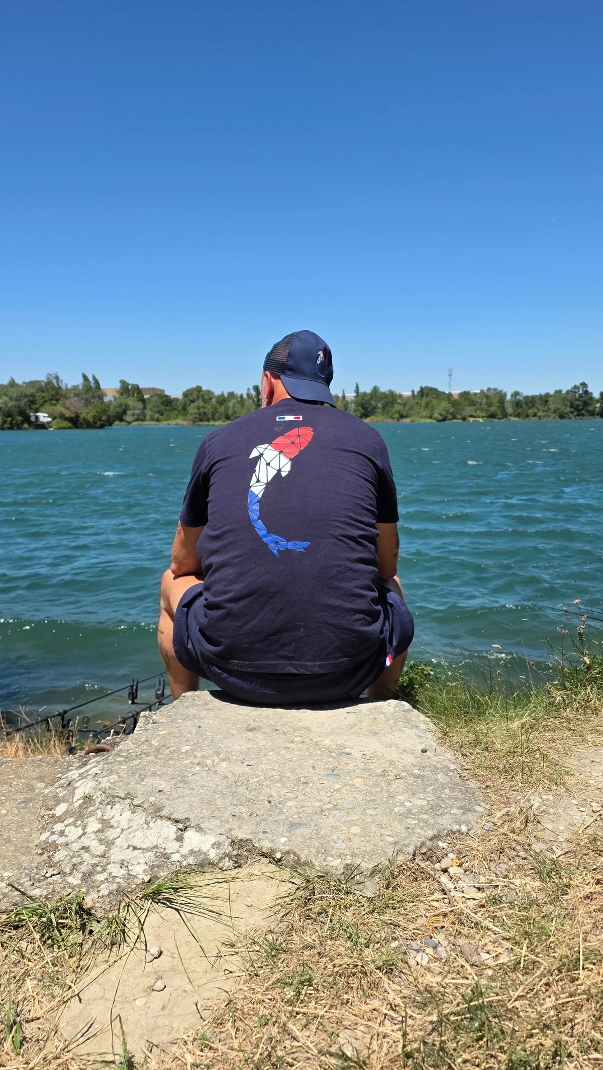 Connected Carper La Frenchie t-shirt with blue, white, and red carp logo worn by a fisherman at the lake