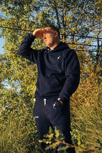 Connected Carper navy blue fishing joggers with tricolor embroidery, worn by a man outdoors at sunset.