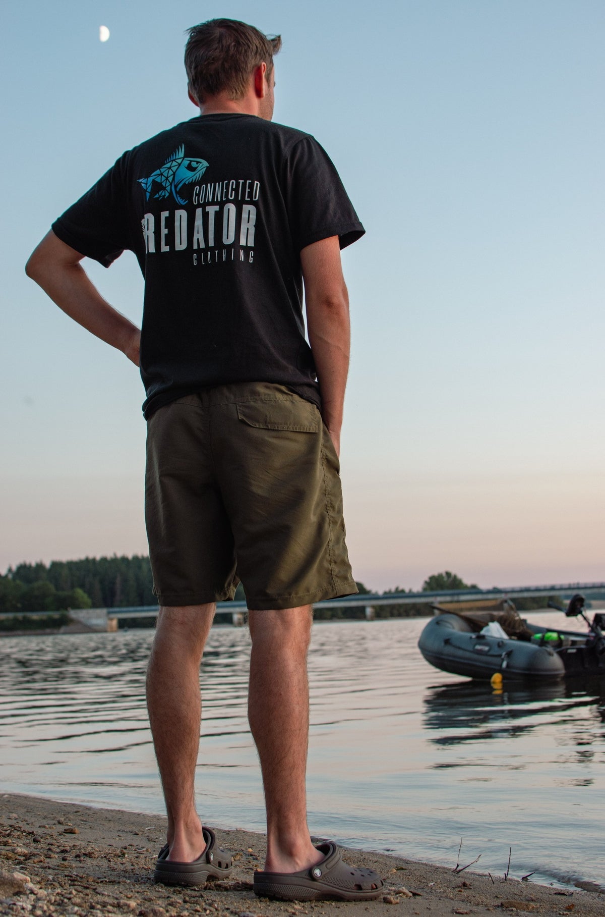 Connected Carper black cotton blend t-shirt with blue and white Predator logo on back, worn by man at the lakeside.