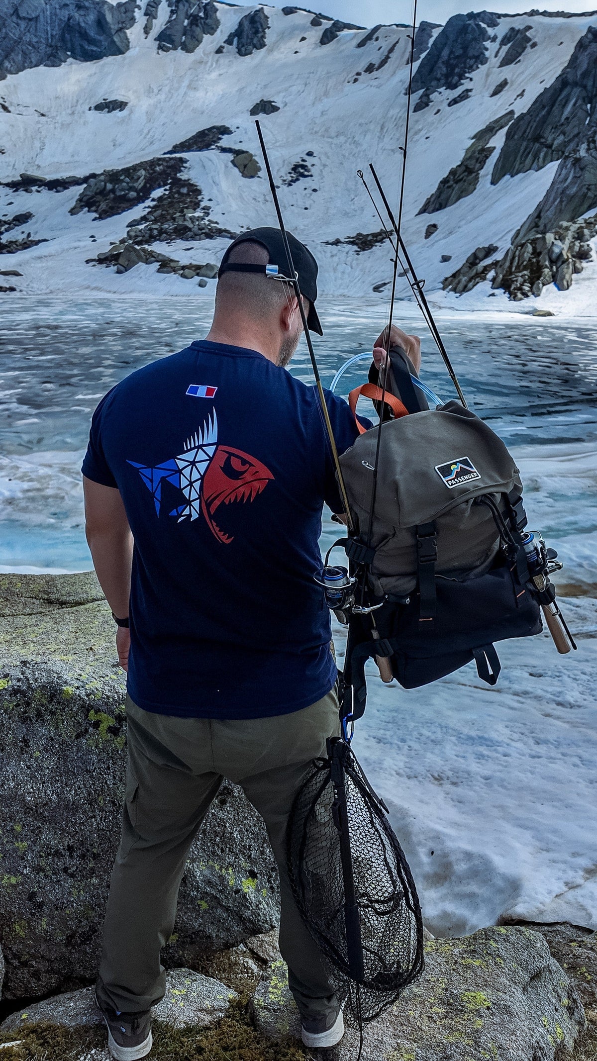 Connected Carper navy blue Predator Frenchie t-shirt with tricolor logo, worn by a fisherman in a snowy mountain area.