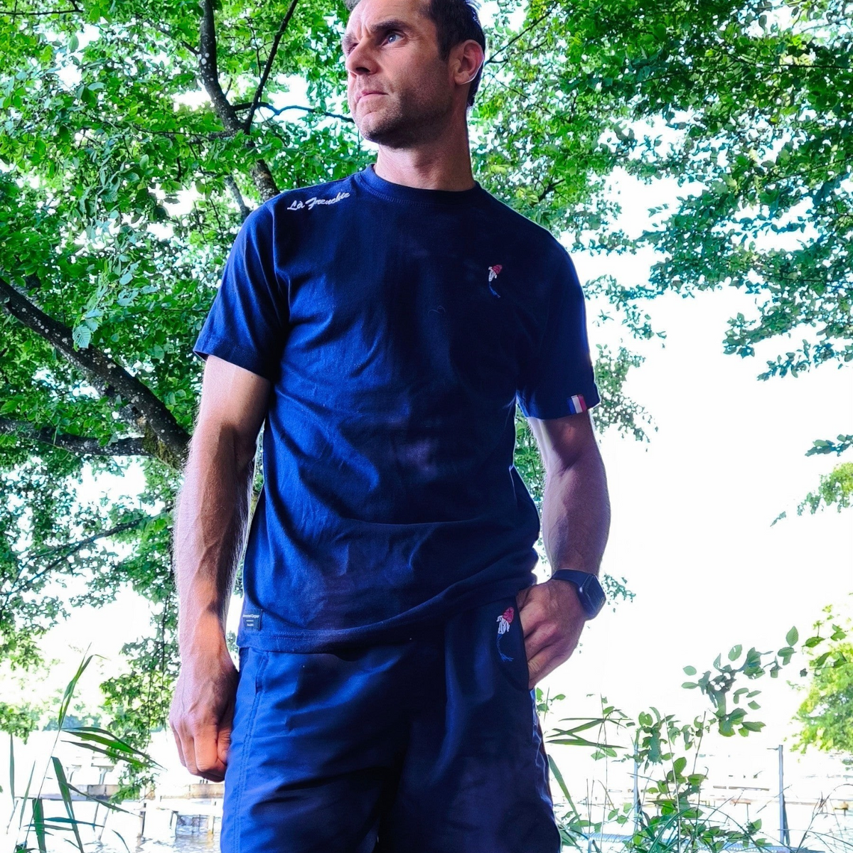 Homme portant le short de bain bleu marine Connected Carper avec détails tricolores au bord d'un lac en été