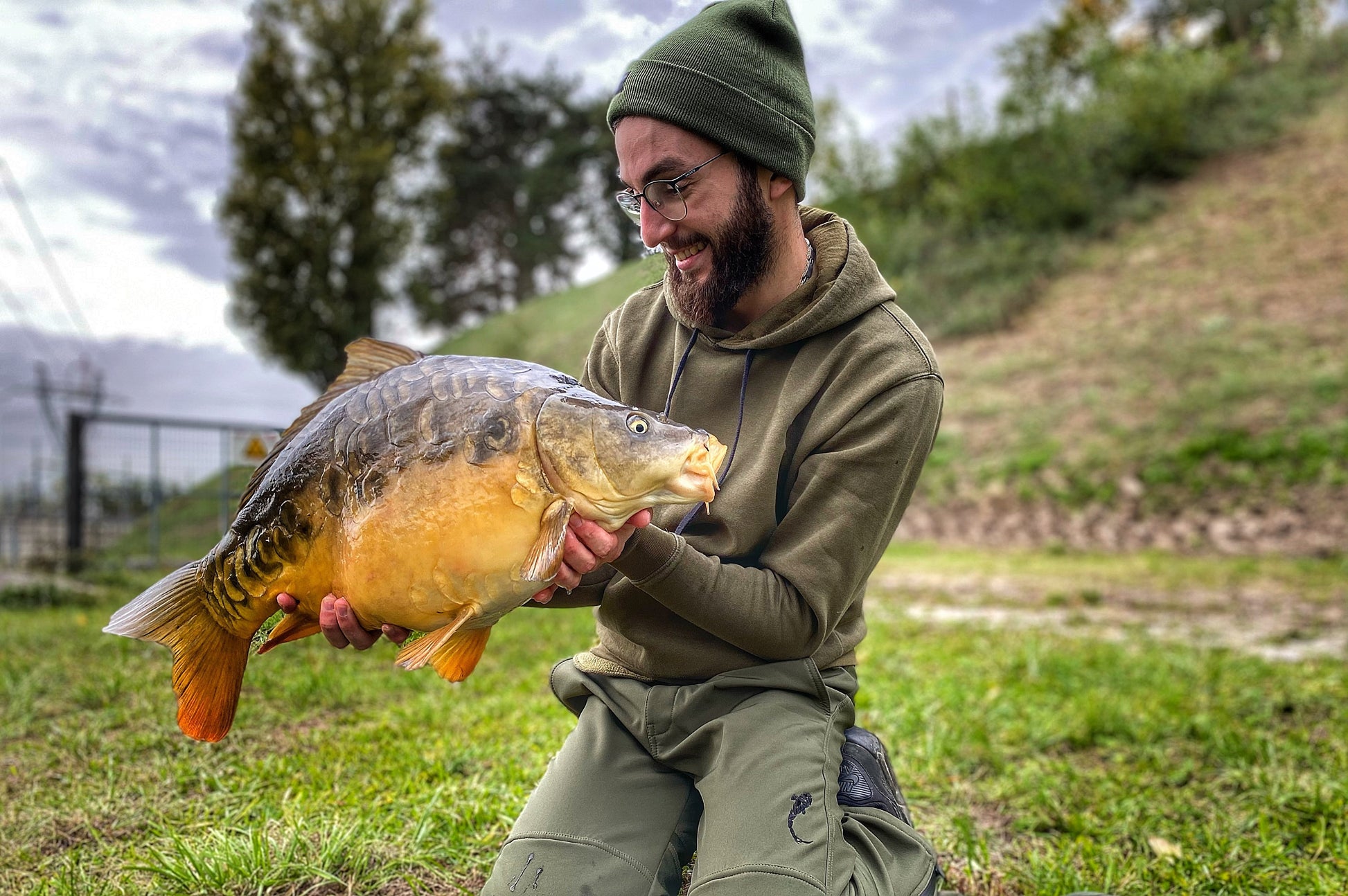 Homme portant un sweat Connected Carper au bord de l’eau pendant une session carpe
