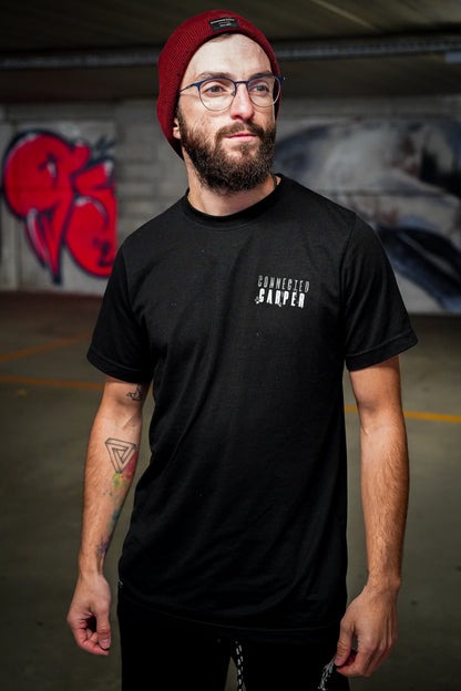 Man wearing a black Connected Carper t-shirt with white chest logo and a burgundy beanie in an urban setting